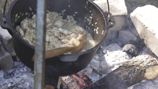 Cooking girolle (Cantharellus cibarius) mushroom and chicken risotto in cast iron pot on an open campfire