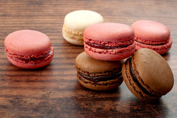 Obraz na płótnie Canvas candy sandwich and french gastronomy conceptual idea with close up on heap of selection of white (vanilla), pink (strawberry), and brown (coffee) macaroon on wood background