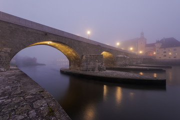 The Stone Bridge in the bavarian city of Regensburg before dawn covered in dense autumn fog