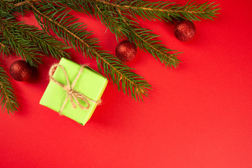 Fototapeta na wymiar Christmas composition. Green gift, branches of spruce, red ornaments on a red background. Christmas, winter, new year concept. Flat lay, top view, copy space