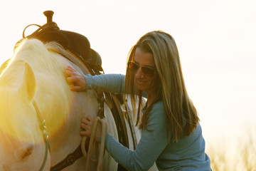 Woman showing love and affection to pet horse close up with sun flare during sunset on ranch.