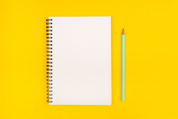 Empty notebook and pencil on yellow background, top view. Copy space.