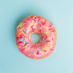 Flat lay of pink donut decorated with sprinkles on blue background