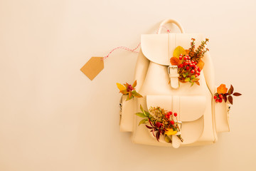 White backpack decorated with autumn leaves and blank tag