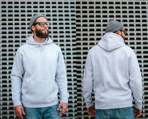 City portrait of handsome hipster guy with beard wearing gray blank hoodie or sweatshirt and hat with space for your logo or design. Mockup for print