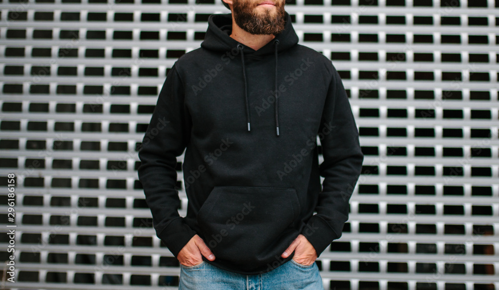 Wall mural city portrait of handsome hipster guy with beard wearing black blank hoodie or sweatshirt and hat wi - Wall murals