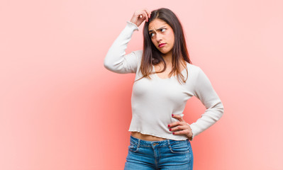 young  pretty woman feeling puzzled and confused, scratching head and looking to the side against pink background. © kues1