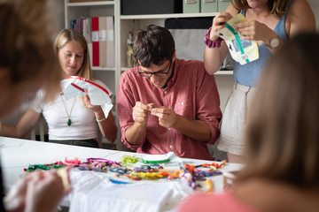 Woman showing a man how to set up his embroidery hoop at a cross-stitching class