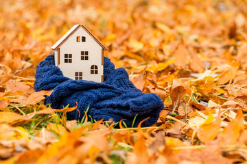 Toy wooden house is wrapped in a warm scarf on the autumn leaves background. Warm house concept
