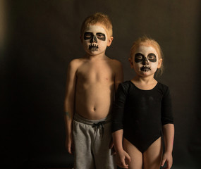  children boy and girl in makeup halloween look at the camera on a dark background