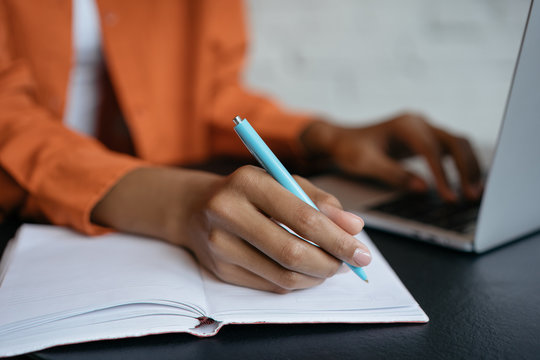 Closeup shot of university student hand using pen and writing in notebook, exam preparation, presentation, working project at workplace. Education concept. Woman taking notes, typing on keyboard 