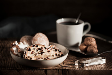 A plate with delicious fresh Christmas stollen and cookies on a rustic wooden board with a cup of tea and biscuits in the background. Christmas concept - Atmospheric dark shot