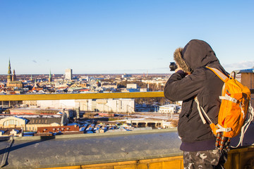Fototapeta premium Photographer with big bag taking picture landmark the ancient european city from a high view point. Latvian Academy of Sciences. Sunny winter day. Riga, Europe, Baltic, Latvia. Travel photos concept