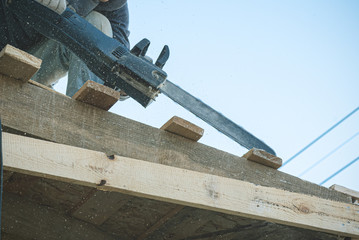 Worker is cutting a wood by a chainsaw.