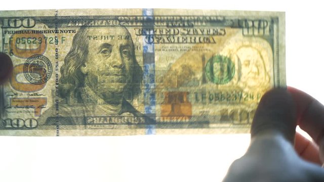 To verify its authenticity a hundred dollar US bill is being inspected closely in the light