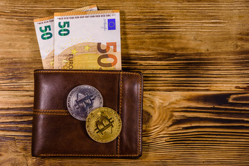 Brown leather wallet with fifty euro banknotes and bitcoins on the wooden background. Top view