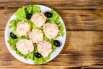White plate with crab-cheese balls, black olives and lettuce leaves on wooden table. Top view