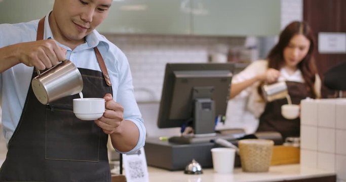 Two Young Asian Barista Man And Woman Making Latte Art At A Coffee Shop.