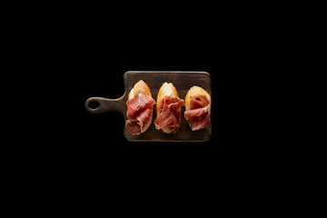 top view of sliced prosciutto on baguette on wooden cutting board isolated on black