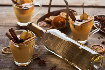 seasonal traditional pear mulled wine with spices in glasses near bottle of white wine on wooden...