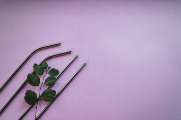 Reusable metallic straws with green leaves on pink background. Eco friendly lifestyle. Copy space.