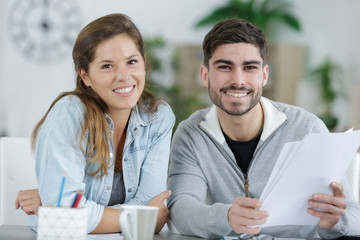 young couple sat at table holding paperwork and smiling