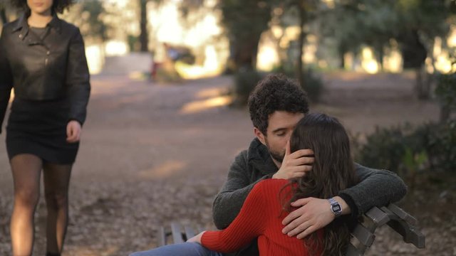 lovers kissing sitting on bench, man  looking other sexy woman walking