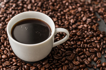 A cup of black coffee on background of roasted coffee beans