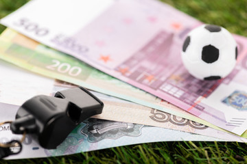selective focus of whistle, toy soccer ball and euro banknotes on green grass, sports betting...