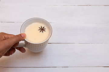 Young woman holding a cup of indian masala tea (chai) decorated with star anise on white wooden table. Image with copy space