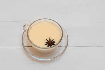 Masala chai, indian traditional spiced milk tea in a glass cup on white wooden table