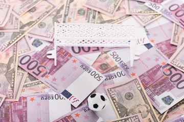 toy soccer ball, miniature football gates on euro and dollar banknotes, sports betting concept