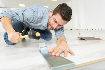 handsome man measuring wooden flooring with hammer
