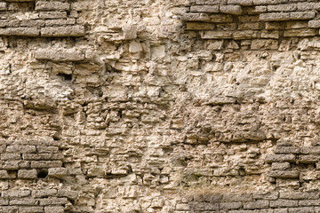 Seamless texture of a sandstone fortified wall with fragments of rectangular blocks of crumbling cladding.