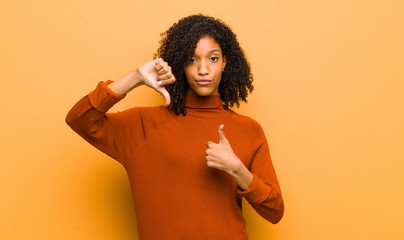 young pretty black woman feeling confused, clueless and unsure, weighting the good and bad in...