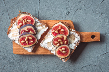 Fig toast with cheese, honey and pine nuts on a wooden board. Rustic breakfast or lunch on a grey...