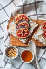 Fig toast with cheese, honey and pine nuts on a wooden board. Rustic breakfast or lunch. Pine nuts, honey and spoon on a white towel top view.