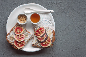 Fig toast with cheese, honey and pine nuts on a white plate. Rustic breakfast or lunch. Pine nuts, honey and spoon on a plate top view. 