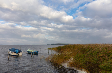 Fototapeta na wymiar A view of the sea and the landscape of the German holiday island Ruegen. Small boats are moored in front of the reeds at their moorings. It is windy and wavy with whitecaps.