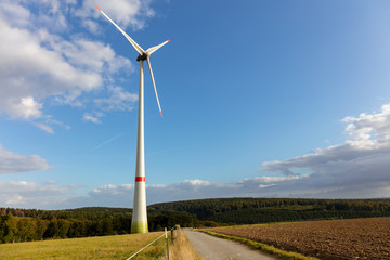 Wind turbine for power generation on a field in Germany. Blue sky, clouds and in the background a forest.