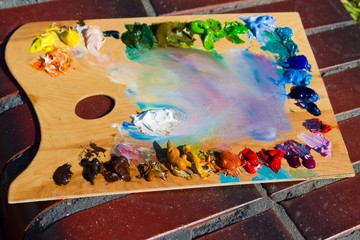 painter's wooden palette with a mix of fresh bright colorful oil paints in disorder at a break during summer plainair painting, artist's creative inspiration in direct sunlight