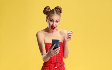Studio shot of Surprised girl looking at smartphone on yellow background
