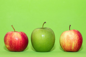 Three apples are arranged on green background. One fruit in the middle green color outstanding other.Food minimal concept