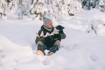 Fototapeta na wymiar Happy man holding lovely dog in his hands in snowy forest. Smiling boy hugging adorable puppy in winter wood. Pet lover. Dog - human`s friend concept.