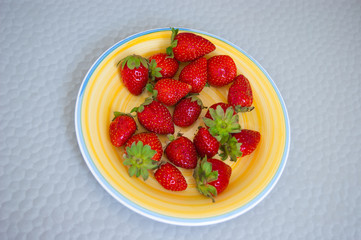 Red berries of garden strawberries with green sepals on a sunny yellow porcelain plate