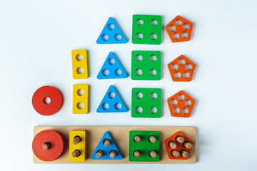 Wooden toy for learning numbers and shapes. Numbers from one to five. Multi-colored figures circle, square, rectangle, triangle, five gon. Child plays Montessori game. Kid collects wooden toy sorter. 