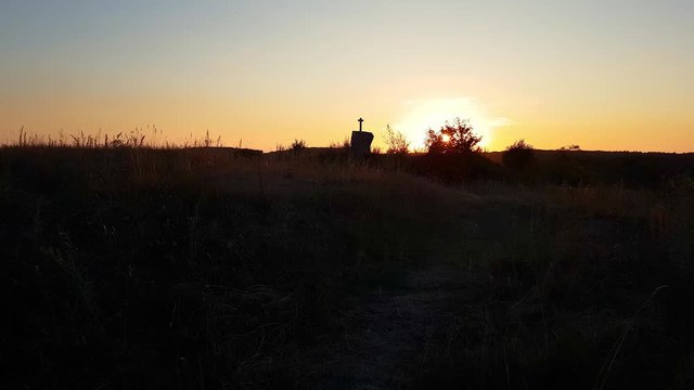 Stone cross on top of a mountain against a sunset. Cross on a sunset background. Stone crem on the mountain at sunset