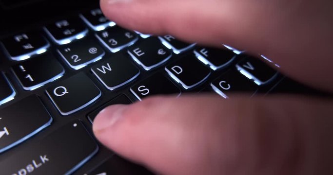 Close up PC gamer playing on gaming laptop with backlit keyboard using WASD keys in a dark room