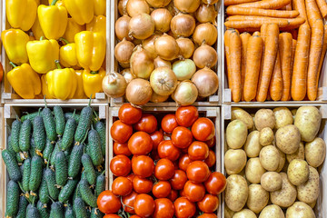 A counter with different vegetables in drawers is beautifully and evenly laid out from above. Carrots Potatoes cucumbers, bell peppers, onions, tomatoes.