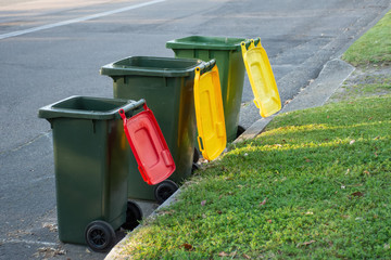 Australian garbage wheelie bins with colourful lids for recycling and general household waste lined up on the street kerbside for council rubbish collection